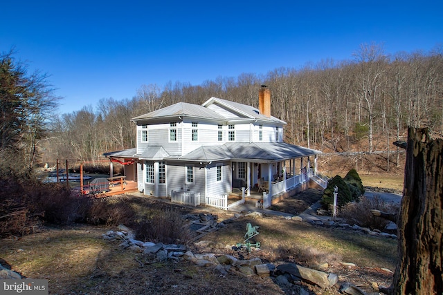 view of front facade featuring a chimney, covered porch, central AC, metal roof, and a forest view