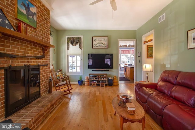 living area featuring a fireplace, wood-type flooring, visible vents, a ceiling fan, and baseboards