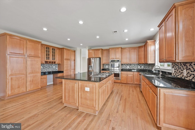 kitchen featuring light wood-style flooring, stainless steel appliances, a kitchen island, a sink, and visible vents