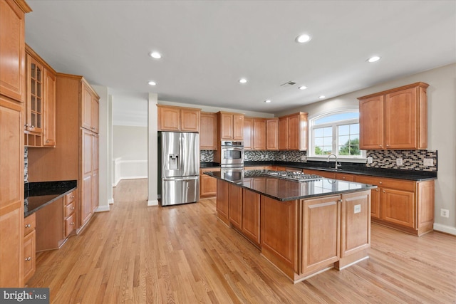 kitchen featuring decorative backsplash, light wood-style flooring, a kitchen island, appliances with stainless steel finishes, and a sink