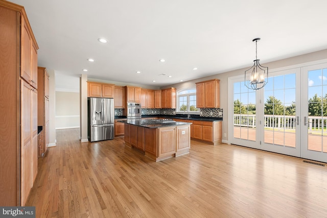 kitchen with stainless steel appliances, visible vents, light wood finished floors, dark countertops, and tasteful backsplash