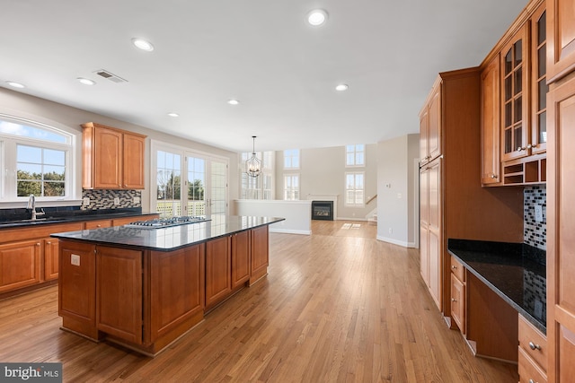 kitchen with light wood finished floors, visible vents, decorative backsplash, glass insert cabinets, and a sink