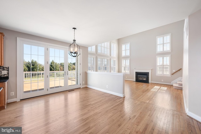 unfurnished dining area featuring an inviting chandelier, a glass covered fireplace, light wood-type flooring, baseboards, and stairs