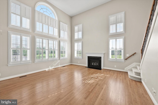 unfurnished living room with a high ceiling, wood finished floors, visible vents, baseboards, and stairway