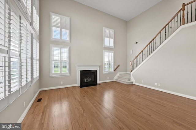 unfurnished living room featuring plenty of natural light, stairs, baseboards, and wood finished floors