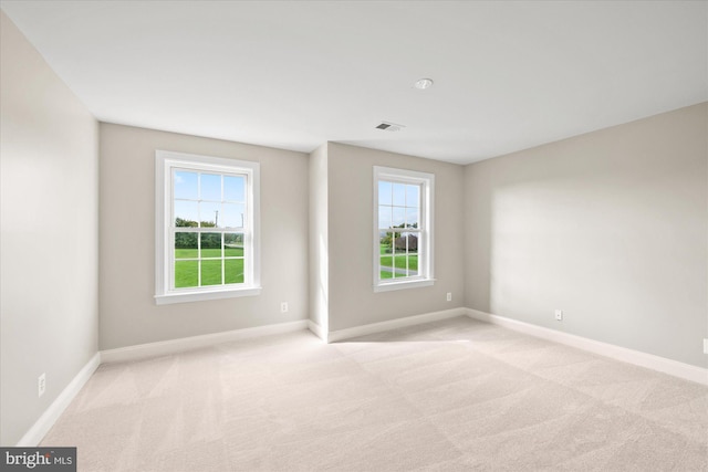 empty room with a wealth of natural light, light carpet, and baseboards