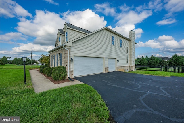 view of side of home featuring a lawn, aphalt driveway, an attached garage, fence, and brick siding