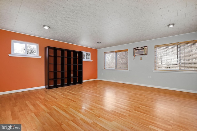 spare room with baseboards, wood finished floors, and a wall unit AC