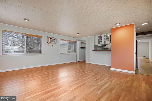 unfurnished living room with a wall unit AC, baseboards, light wood-type flooring, and a wealth of natural light