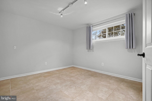 spare room with track lighting and baseboards