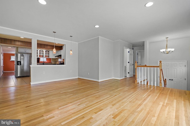 unfurnished living room with a notable chandelier, wood finished floors, recessed lighting, crown molding, and baseboards