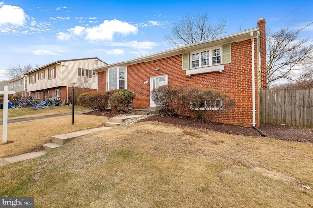 view of front facade with a front yard, fence, brick siding, and a chimney