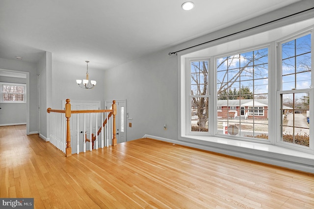 unfurnished room with baseboards, a notable chandelier, and wood finished floors