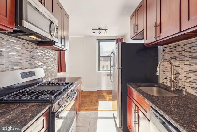 kitchen with appliances with stainless steel finishes, light tile patterned flooring, a sink, and decorative backsplash