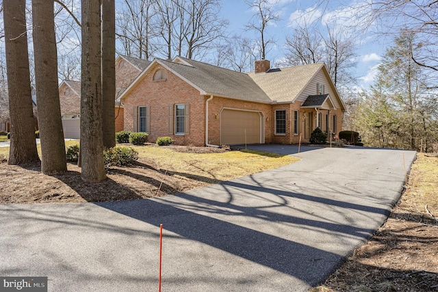 view of front of home featuring an attached garage, brick siding, driveway, and a chimney