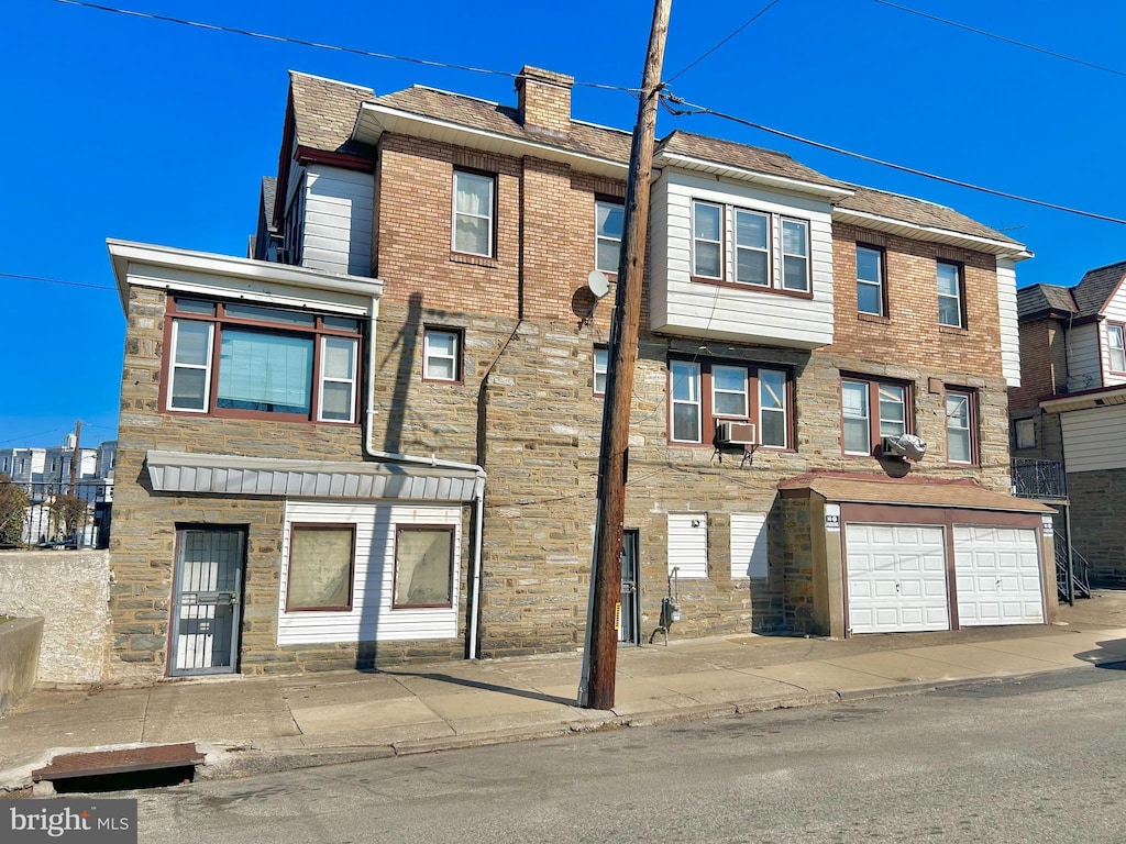 multi unit property with a garage, cooling unit, stone siding, and a chimney