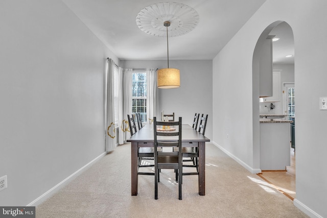 dining room featuring baseboards, arched walkways, and light colored carpet