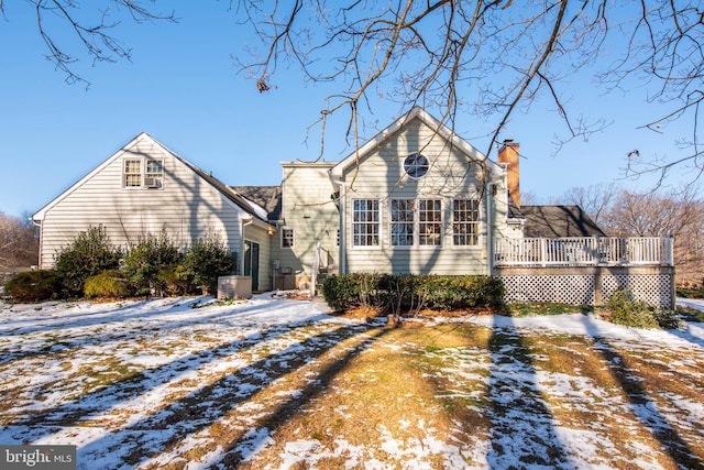 snow covered rear of property with central AC unit, a chimney, and a wooden deck