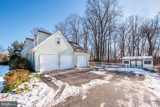 view of snowy exterior with driveway, fence, and an outbuilding