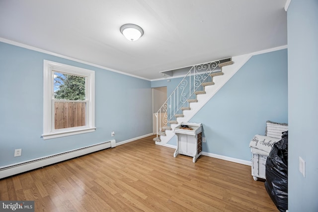 spare room featuring crown molding, stairway, a baseboard heating unit, wood finished floors, and baseboards