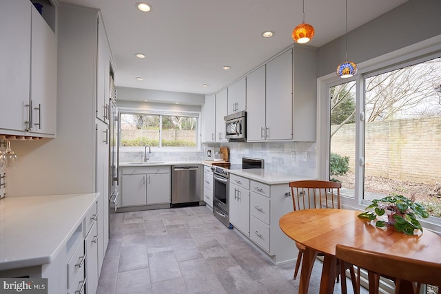 kitchen with backsplash, decorative light fixtures, stainless steel appliances, light countertops, and a sink