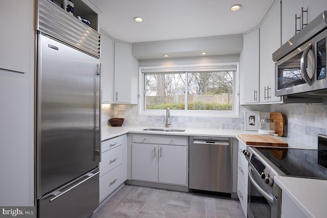 kitchen with light countertops, decorative backsplash, appliances with stainless steel finishes, white cabinetry, and a sink