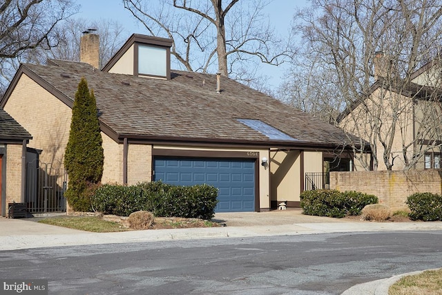 view of front facade featuring brick siding, a chimney, concrete driveway, fence, and a garage