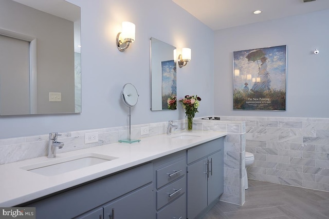 full bathroom featuring a wainscoted wall, double vanity, a sink, and tile walls