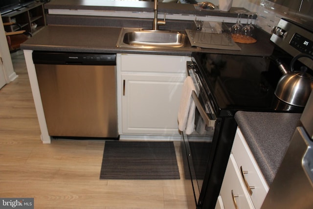 kitchen featuring a sink, white cabinets, light wood-style floors, appliances with stainless steel finishes, and dark countertops