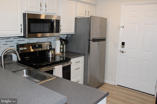 kitchen with light wood-type flooring, tasteful backsplash, dark countertops, white cabinetry, and stainless steel appliances