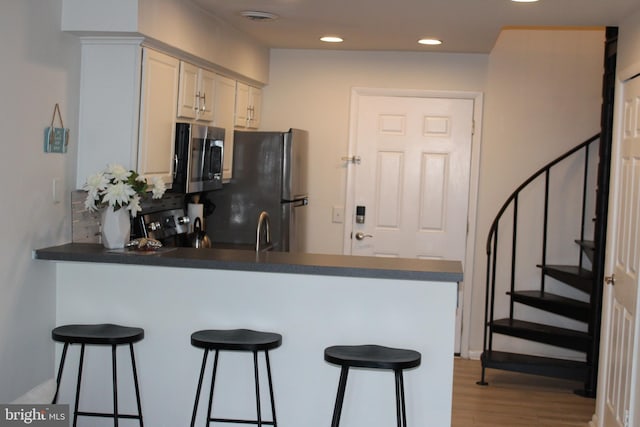 kitchen featuring light wood finished floors, a peninsula, recessed lighting, appliances with stainless steel finishes, and a kitchen breakfast bar