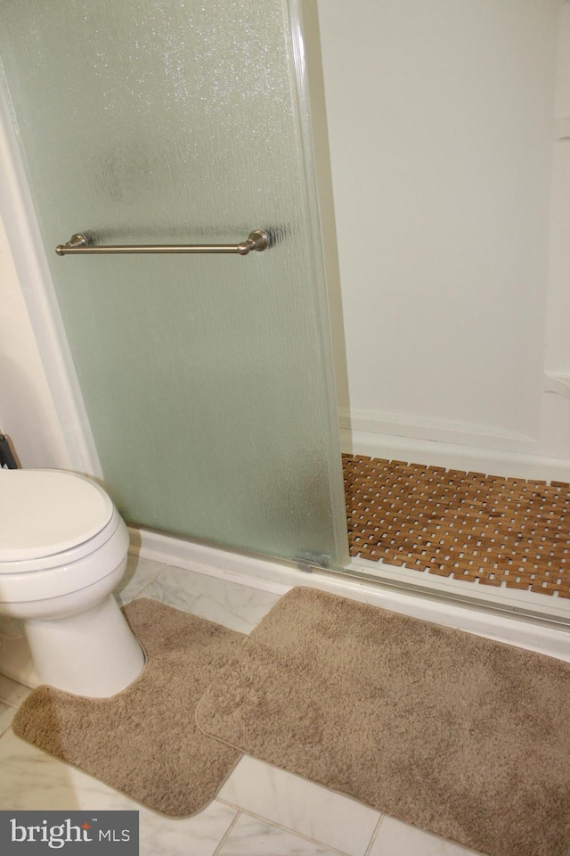 bathroom featuring toilet, baseboards, a stall shower, and marble finish floor