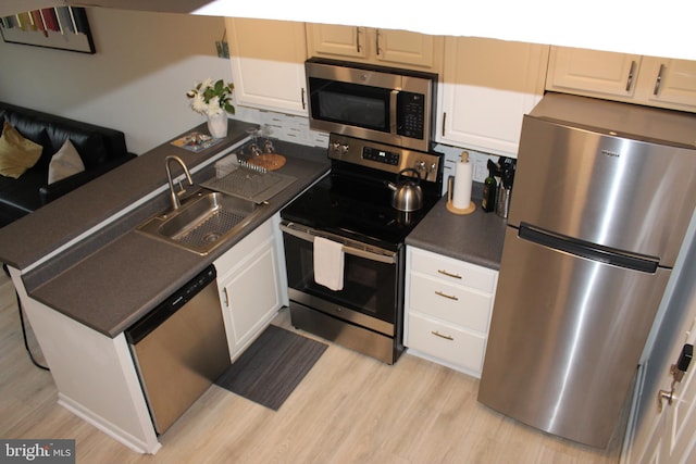 kitchen featuring a sink, dark countertops, appliances with stainless steel finishes, white cabinets, and light wood finished floors