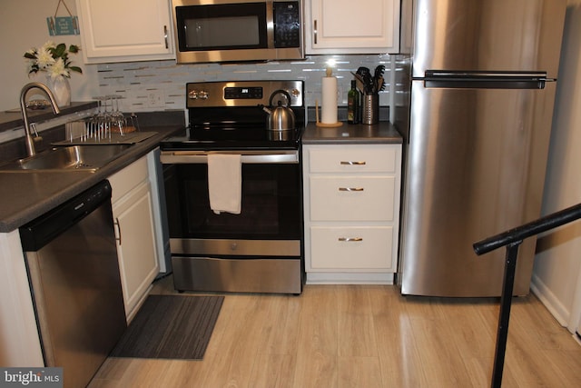 kitchen featuring a sink, appliances with stainless steel finishes, white cabinetry, dark countertops, and light wood-type flooring