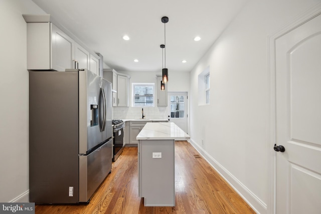 kitchen featuring light wood-style flooring, stainless steel appliances, a kitchen island, baseboards, and decorative backsplash