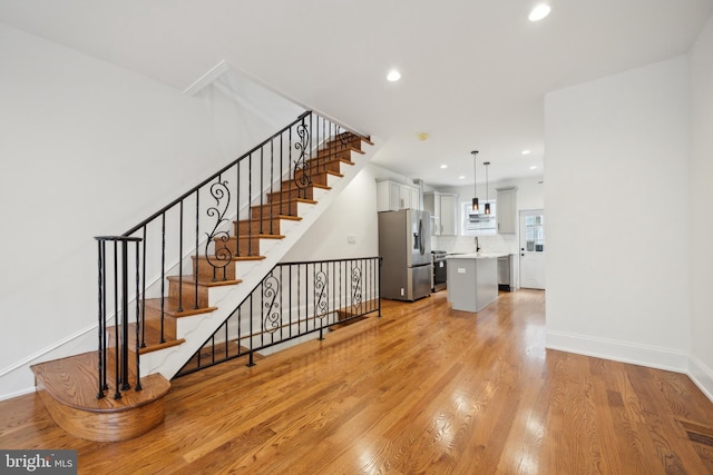 unfurnished living room featuring baseboards, stairway, recessed lighting, and light wood-style floors