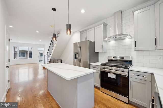 kitchen featuring decorative backsplash, light wood-style floors, appliances with stainless steel finishes, a center island, and wall chimney range hood