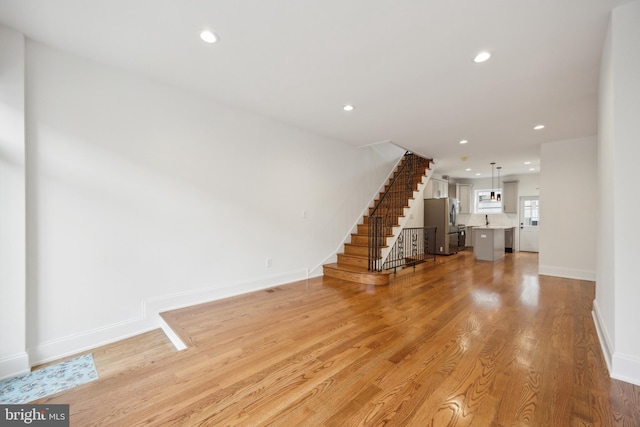 unfurnished living room featuring stairs, light wood finished floors, baseboards, and recessed lighting