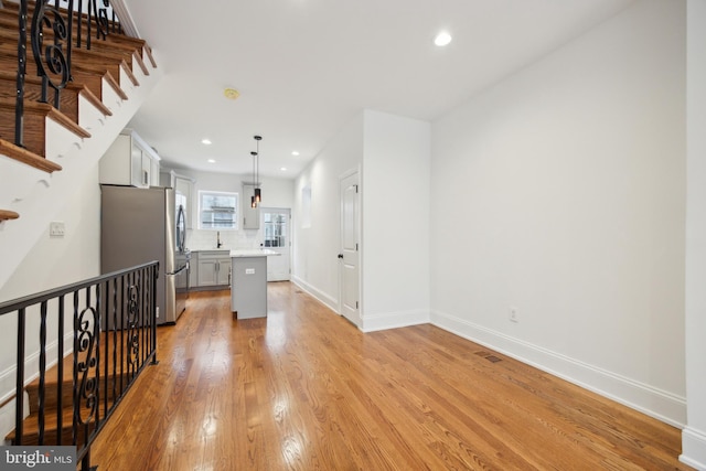 kitchen with light countertops, light wood-type flooring, backsplash, freestanding refrigerator, and a center island