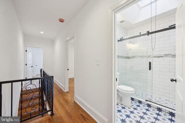 full bath with a skylight, baseboards, toilet, wood finished floors, and a shower stall