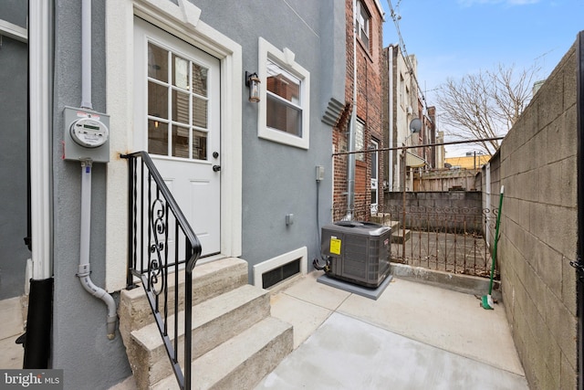 view of exterior entry featuring central AC, fence, and stucco siding