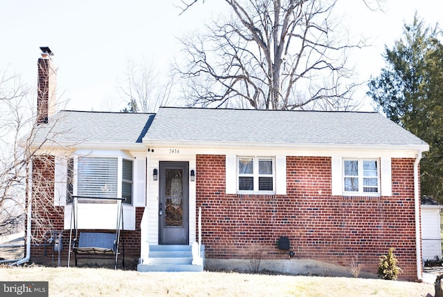 view of front facade with entry steps, roof with shingles, brick siding, and a chimney