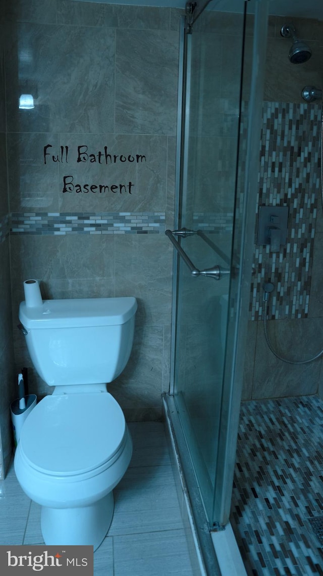 bathroom with tile patterned floors, a shower stall, tile walls, and toilet