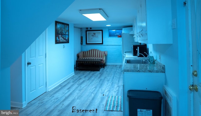 kitchen with white cabinets, baseboards, light wood-type flooring, and a sink