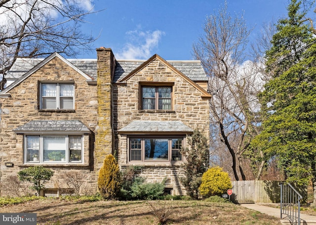 view of front of house featuring a high end roof, stone siding, fence, and a chimney