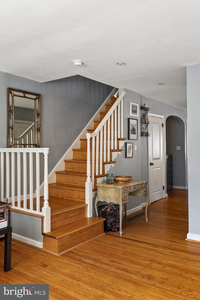 stairway with arched walkways, wood finished floors, and baseboards