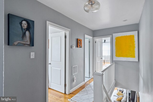 corridor with light wood-style floors, visible vents, an upstairs landing, and baseboards