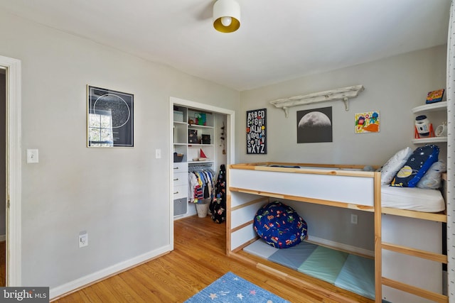 bedroom with a closet, baseboards, a walk in closet, and wood finished floors