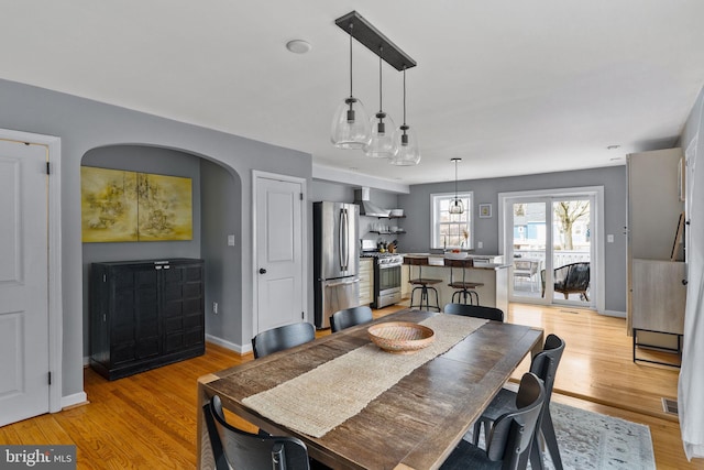 dining area featuring arched walkways, baseboards, visible vents, and light wood finished floors