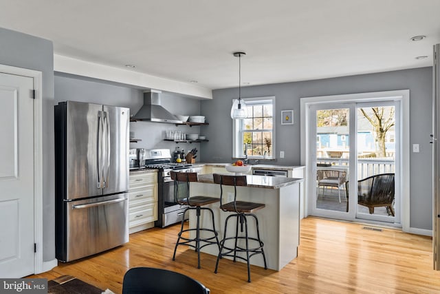 kitchen with a breakfast bar, visible vents, appliances with stainless steel finishes, light wood-style floors, and wall chimney range hood